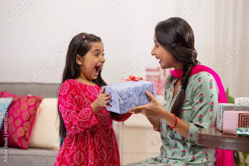 A daughter overjoyed at gift given by mother amidst other presents kept in room. photo
