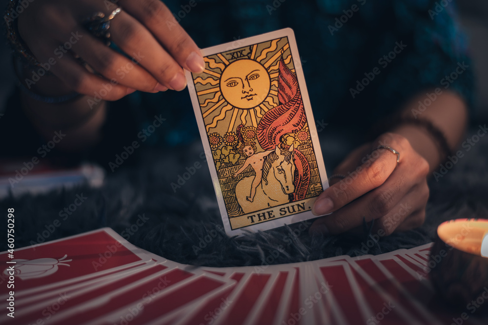 Fortune teller holding THE SUN card and tarot cards. tarot cards and burning candles. Astrologists and forecasting concept. - obrazy, fototapety, plakaty 