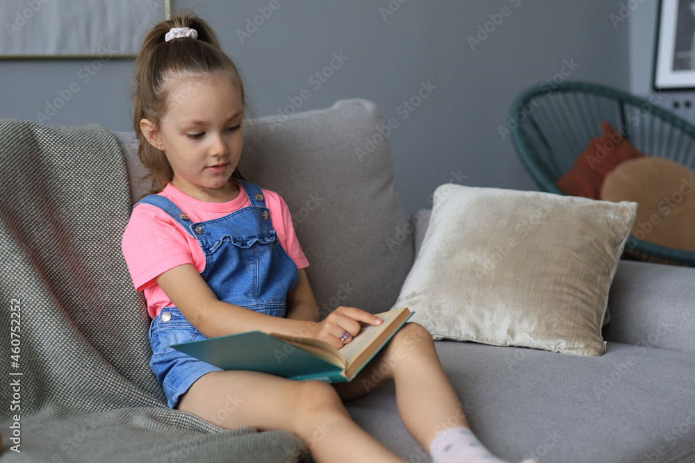 Little girl sits at home and does homework, self study of the material, reading book. The concept of distance education. Little girl sits at home and does homework, self study of the material, reading book. The concept of distance education.