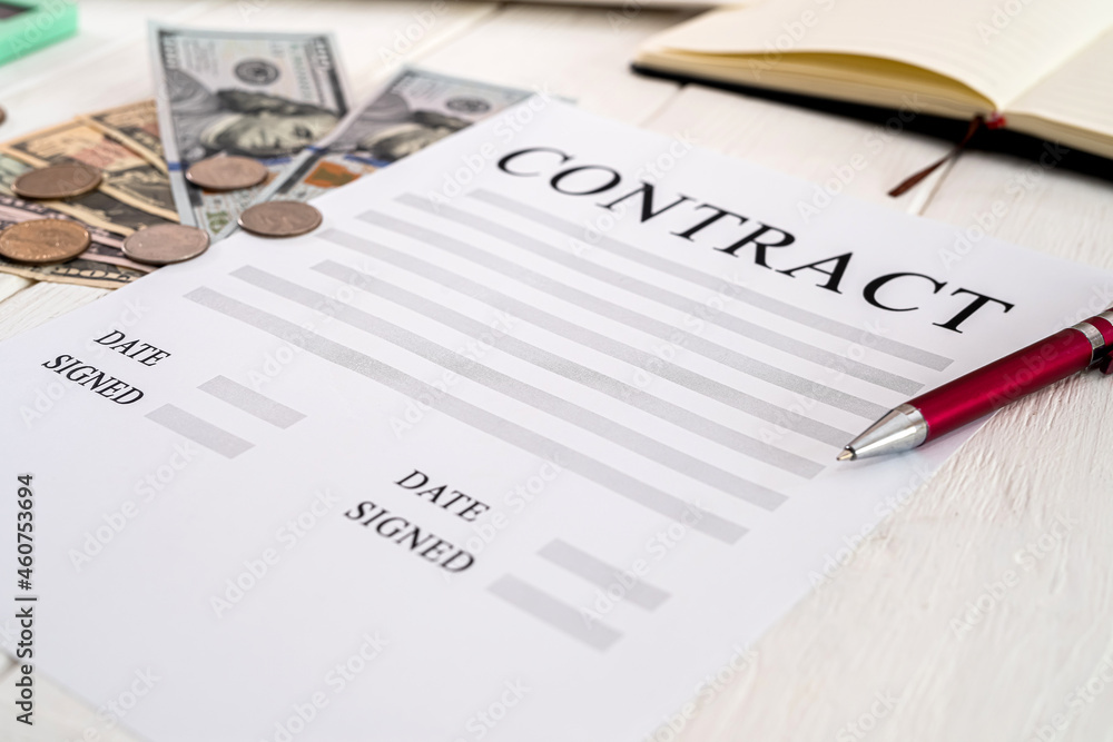 contract with pen and dollar bills lie on a wooden table