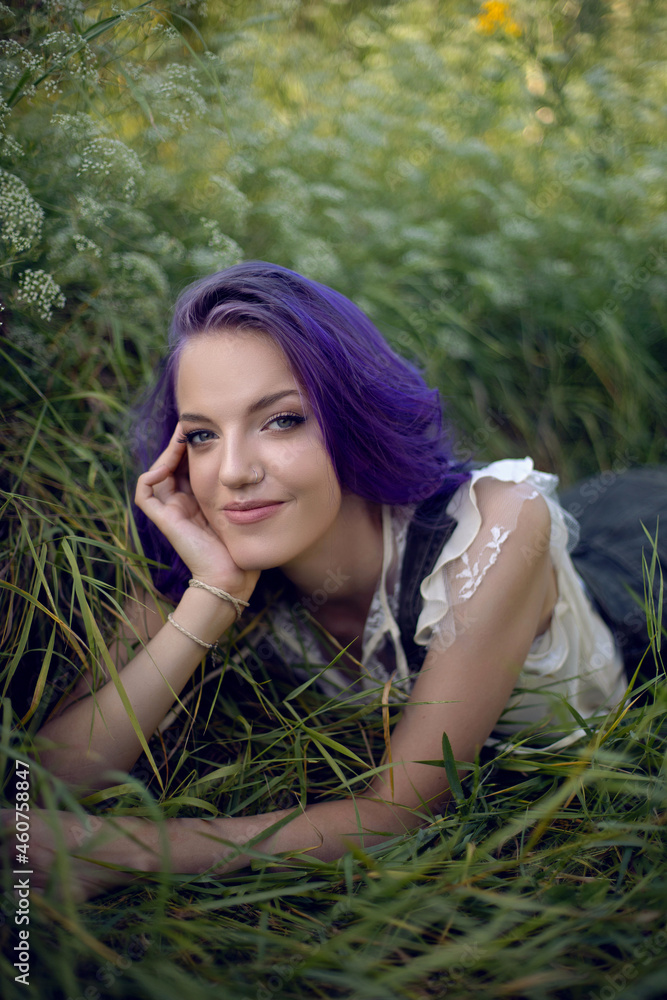 portrait of a teenage girl with purple hair and an earring in her nose lying in the grass portrait of a teenage girl with purple hair and an earring in her nose lying in the grass