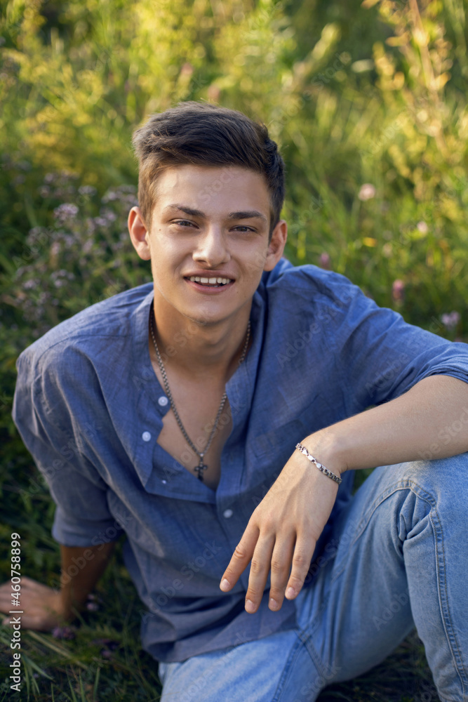 sexy teen guy sitting on the grass in nature in a shirt and jeans sexy teen guy sitting on the grass in nature in a shirt and jeans