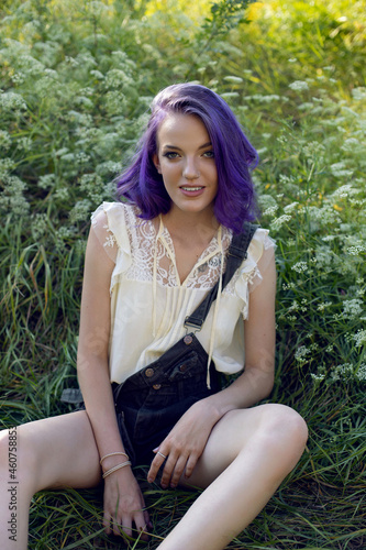 portrait of a teenage girl with purple hair and an earring in her nose sit in the grass