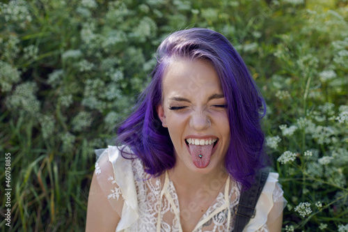 portrait of a teenage girl with purple hair and an earring in her nose sit in the grass photo