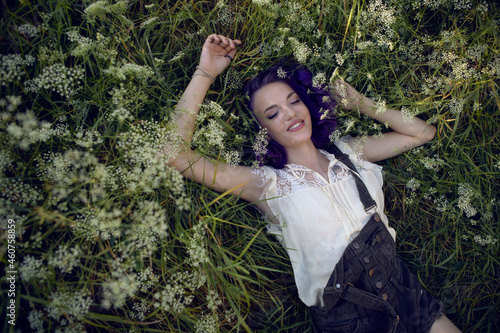 portrait of a teenage girl with purple hair and an earring in her nose lying in the grass