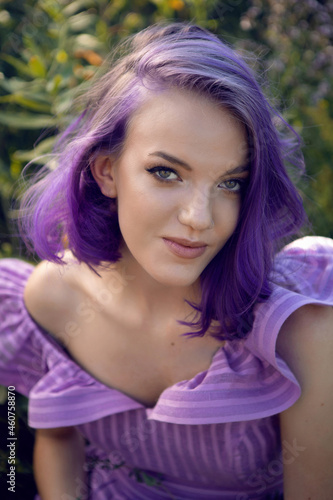 teenage girl with dyed purple hair and a nose piercing in the grass with a bouquet