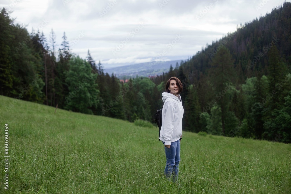 Woman traveler standing on a glade high in the mountains in front of forest, space for text, atmospheric epic moment Woman traveler standing on a glade high in the mountains in front of forest, space for text, atmospheric epic moment
