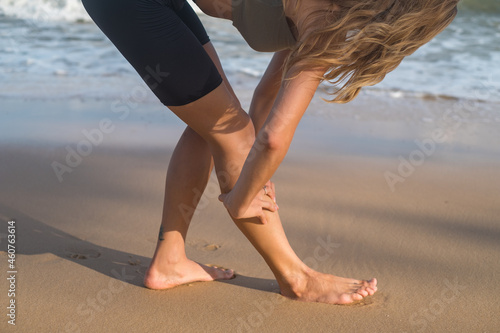 Kneading body muscles after jogging. Blond caucasian Girl massage her leg after jogging on the beach. close up picture, copy space, leg injury