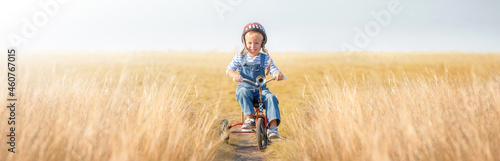 Little boy rides a bicycle. A cheerful, happy child imagines himself a cyclist and plays outdoors against a blue sky on a summer day. Games, dreams of competition in retro style.