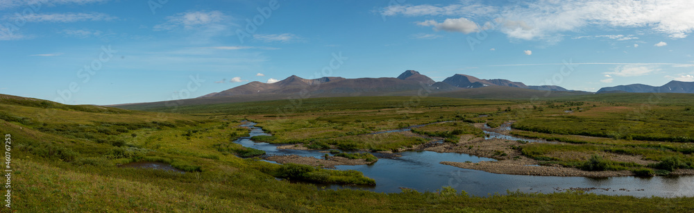 A clear river with rocks leads to the mountains. Clear summer day. Wildlife travel concept.