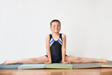 Little boy gymnast is sitting in split on white background