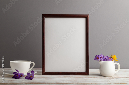 Brown wooden frame mockup with snowdrop crocus flowers and white coffee cup on gray paper background. still life, copy space.