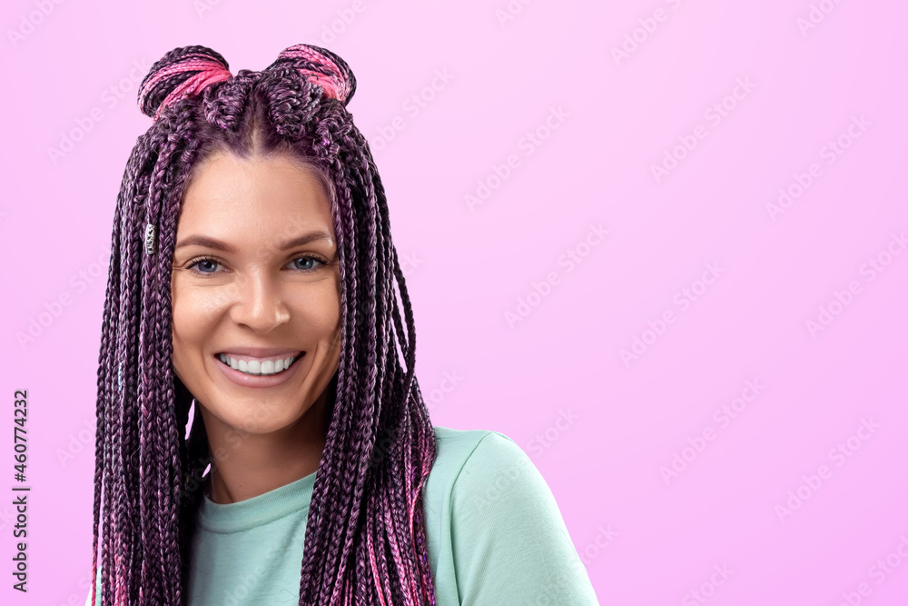 Beautiful girl with a hairstyle of pink braids in turquoise clothes smiles and poses on a pink background in the studio. The concept is modern style, individuality, inclusiveness, creativity. Beautiful girl with a hairstyle of pink braids in turquoise clothes smiles and poses on a pink background in the studio. The concept is modern style, individuality, inclusiveness, creativity.