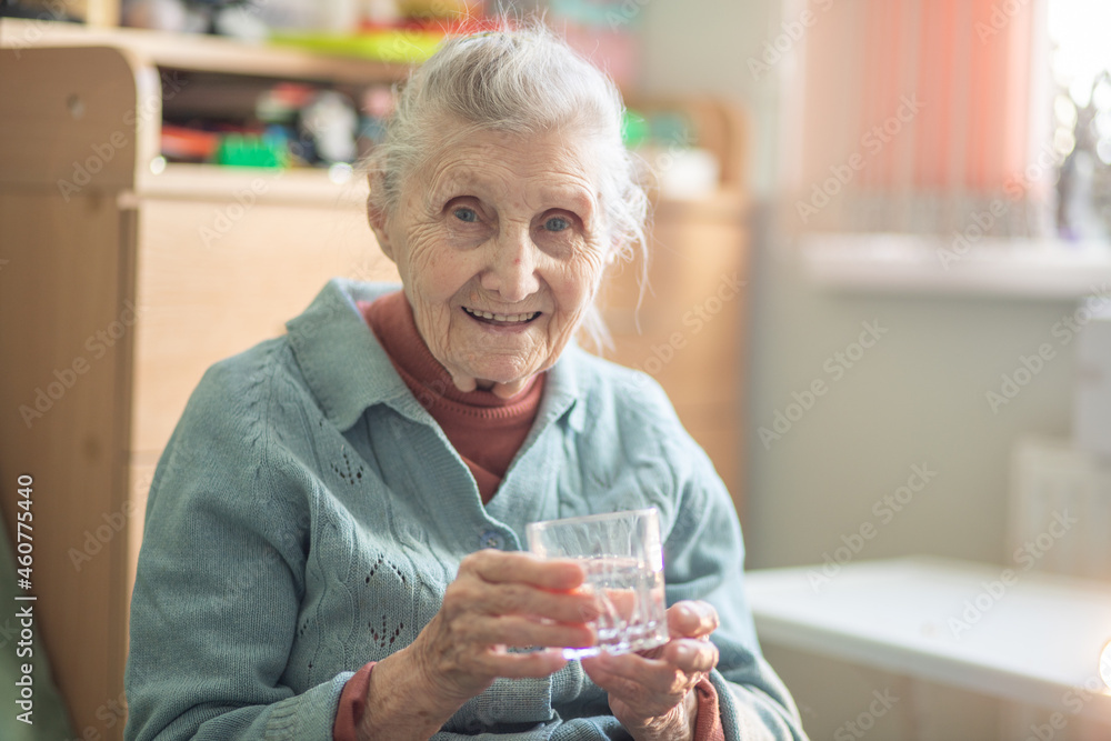 An elderly woman holds a glass glass with water in her hand, health care, grandmother drinks water for health, retirees at home during quarantine.
 - obrazy, fototapety, plakaty 