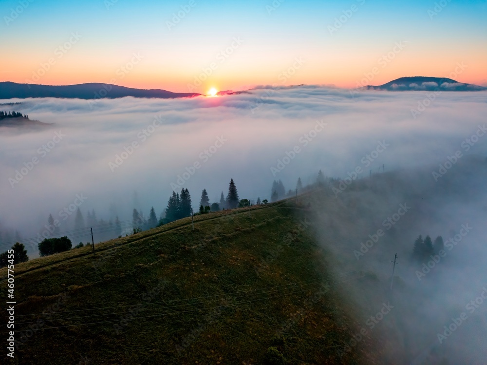 Fog spreads over the mountains at dawn. The sun rises on the horizon. Ukrainian Carpathians in the morning. Aerial drone view.