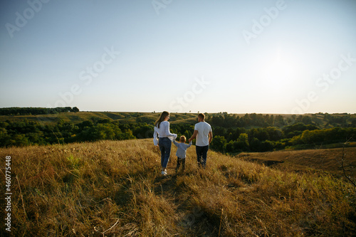 mom and dad run across the field holding their son's hands © Andrii