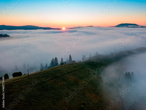 Fog spreads over the mountains at dawn. The sun rises on the horizon. Ukrainian Carpathians in the morning. Aerial drone view.