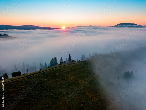 Fog spreads over the mountains at dawn. The sun rises on the horizon. Ukrainian Carpathians in the morning. Aerial drone view.