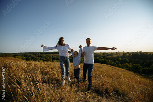 mom and dad run across the field holding their son's hands