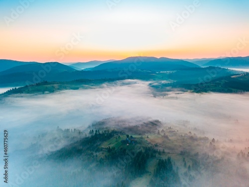 Fog spreads over the mountains at dawn. The sun rises on the horizon. Ukrainian Carpathians in the morning. Aerial drone view.