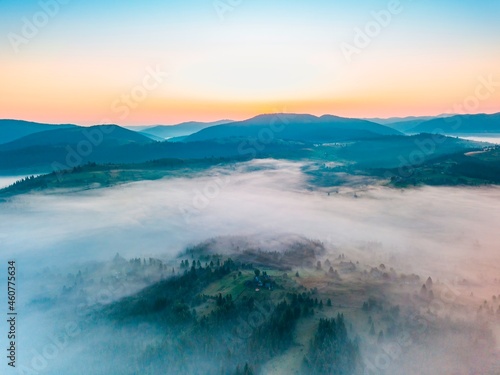 Fog spreads over the mountains at dawn. The sun rises on the horizon. Ukrainian Carpathians in the morning. Aerial drone view.