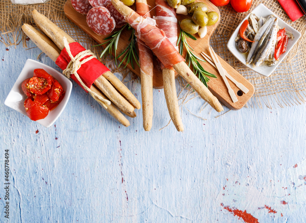 Grissini with smoked ham. Appetizer platter, grissini with smoked ham and olives, salami, anchovy, and dried tomatoes on the side. Top view.