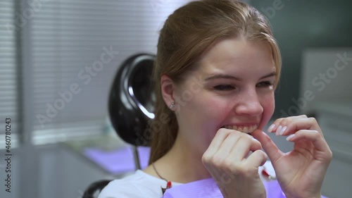 Patient trying on aligners and smiling, sitting in clinic office during orthodontic treatment spbas. Close-up view of young European female inserts transparent sample into her mouth and looks with photo