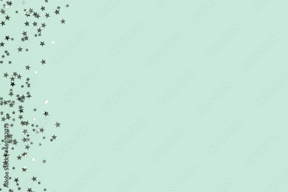 Glowing silver colored glittering stars confetti scattered on a turquoise background with place for text. Glowing silver colored glittering stars confetti scattered on a turquoise background with place for text.