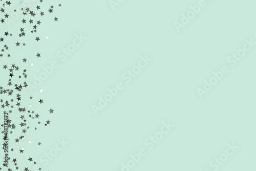 Glowing silver colored glittering stars confetti scattered on a turquoise background with place for text.