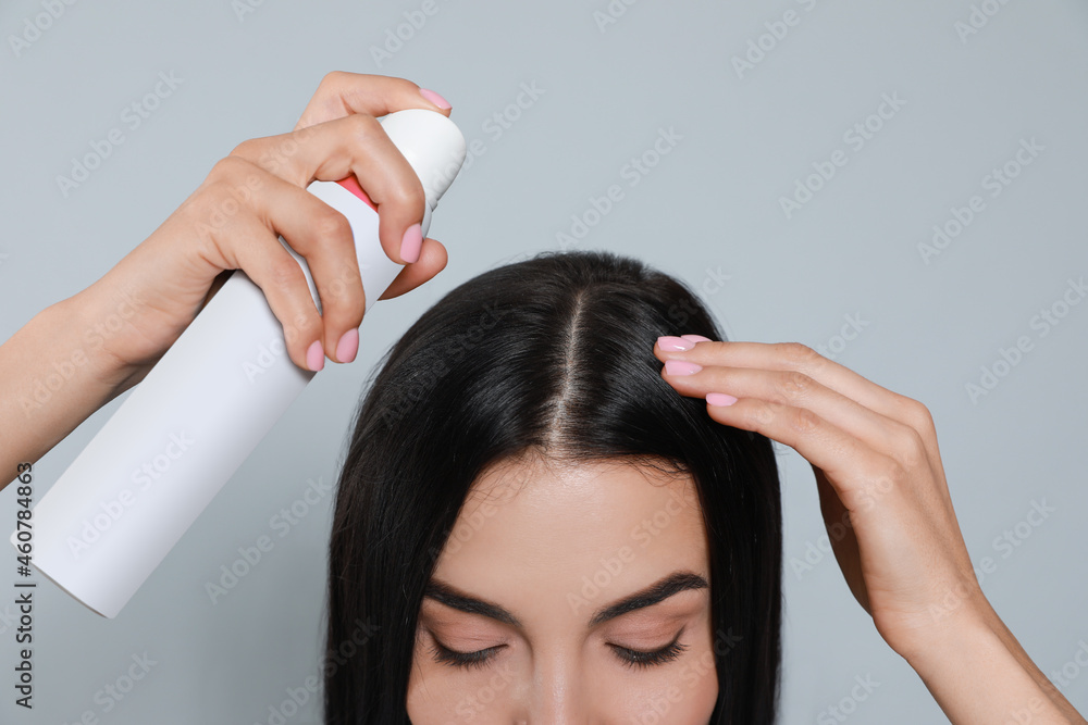 Fototapeta premium Woman applying dry shampoo onto her hair on light grey background, closeup
