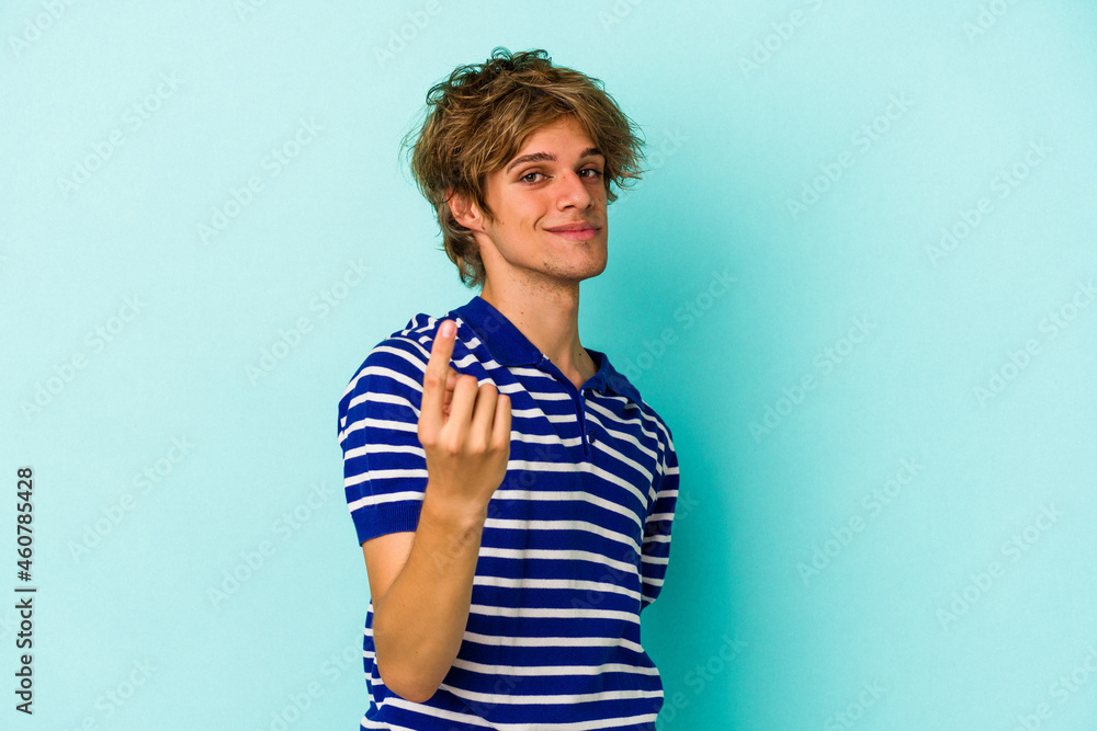 Young caucasian man with make up isolated on blue background pointing with finger at you as if inviting come closer. Young caucasian man with make up isolated on blue background pointing with finger at you as if inviting come closer.