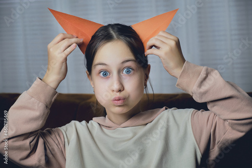 A close-up portrait of a girl in the room makes a face with her red carved ears to her head and bulging eyes.