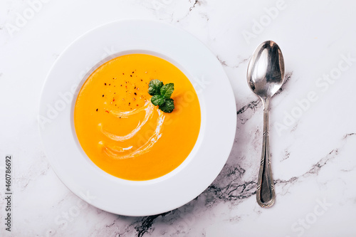 Flat lay of pumpkin soup on white background with cream and mint garnish