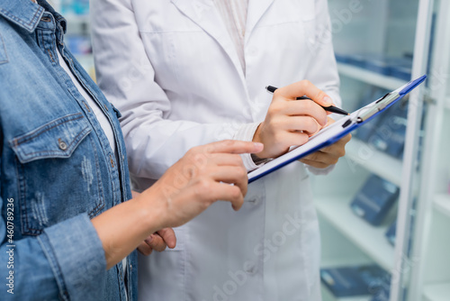 cropped view of customer pointing at clipboard near pharmacist