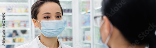 tattooed pharmacist in medical mask looking at blurred colleague, banner