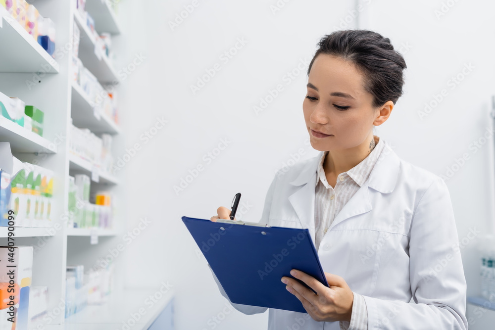 tattooed pharmacist in white coat writing on clipboard in drugstore tattooed pharmacist in white coat writing on clipboard in drugstore