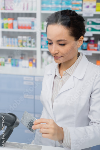 tattooed pharmacist holding blister pack near scanner in drugstore