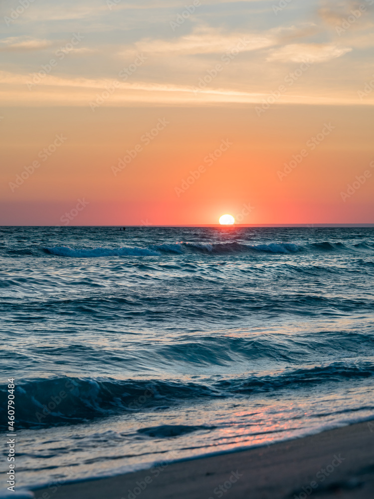 Fototapeta premium Scenic landscape. Sunset over the sea with waves. Orange-pink sky with clouds. Water texture. Vertically