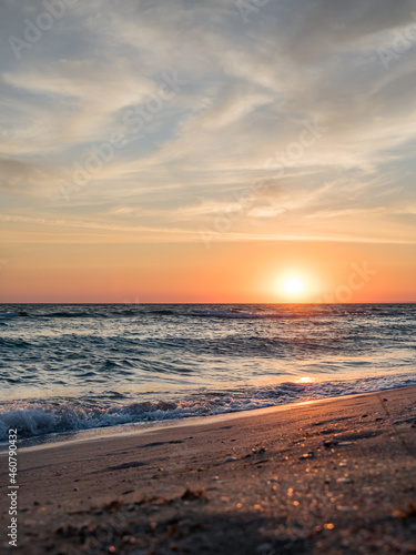 Beautiful, picturesque seascape. Sunset over the ocean. Big waves, clouds, sandy beach with shells. Vertically