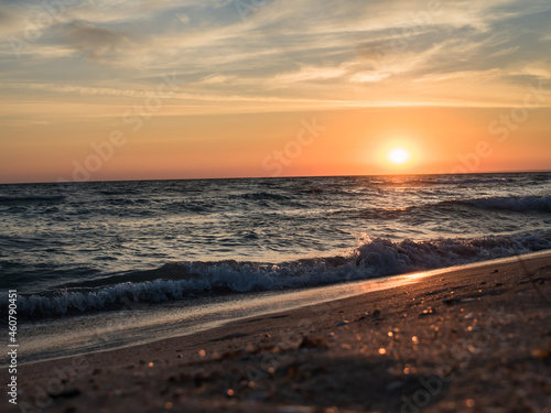 Picturesque landscape. Sunset over the sea. There are clouds in the sky. Sandy coastline. Beautiful big waves. Horizontally
