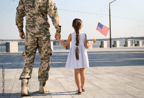 Foto Soldier and his little daughter with American flag outdoors, back view