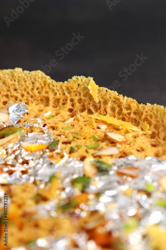 Rajasthani Ghevar. Ghewar is an Indian crunchy sweet dish made using refined flour, sugar, and ghee. Garnished with silver foil and dry fruits. Over dark background with copy space. photo