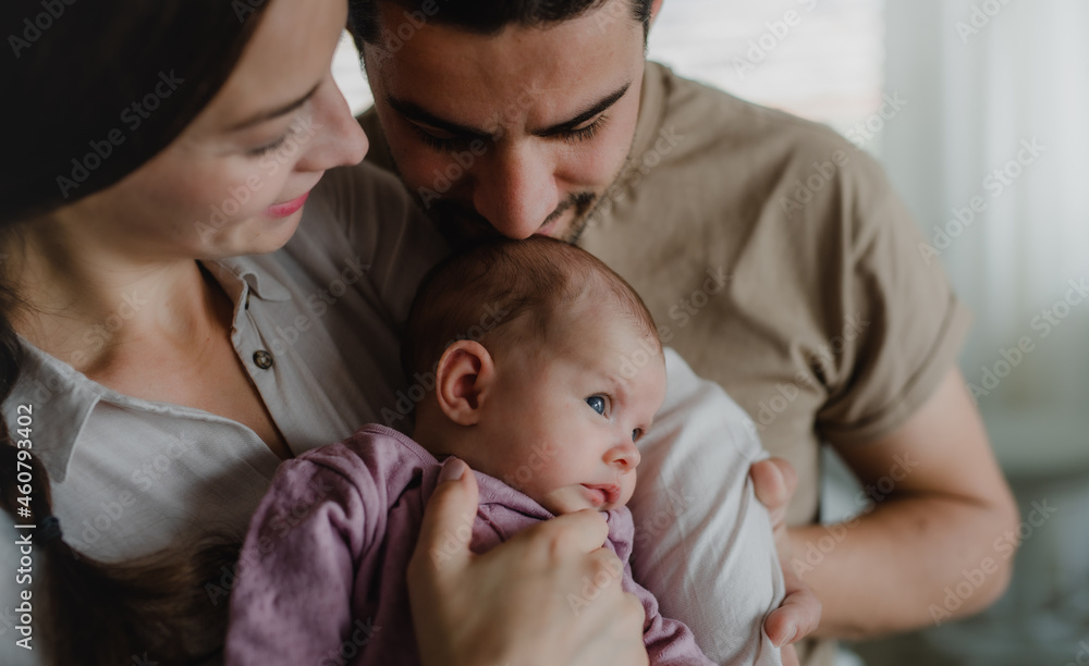 Close up of young parents holding and kissing their newborn baby indoors at home Close up of young parents holding and kissing their newborn baby indoors at home