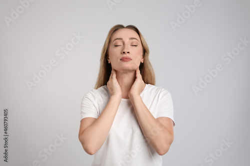 Young woman doing thyroid self examination on light grey background photo