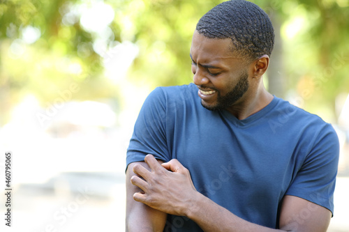 Black man scratching itchy arm in a park