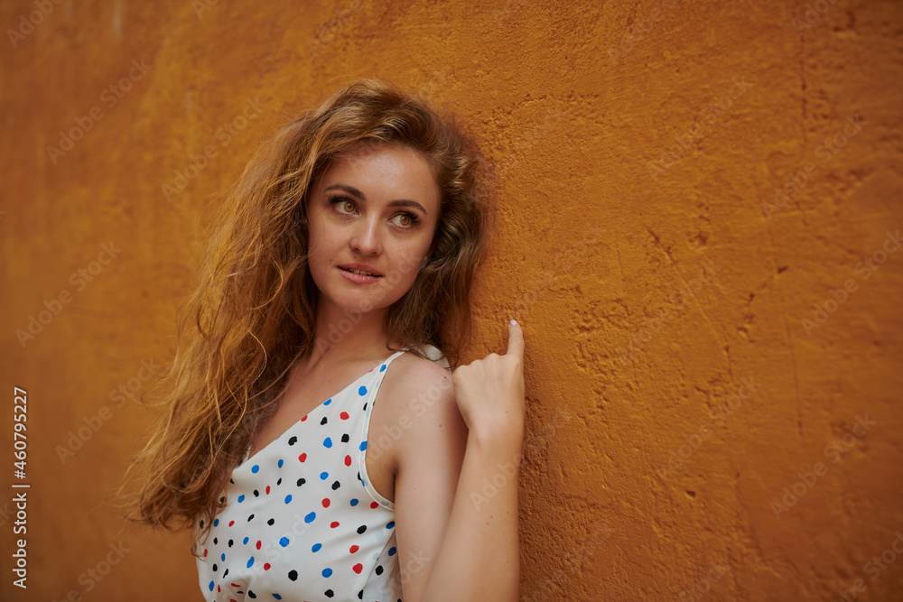Fototapeta premium Portrait of young woman with orange hair on the street with an orange wall as a background