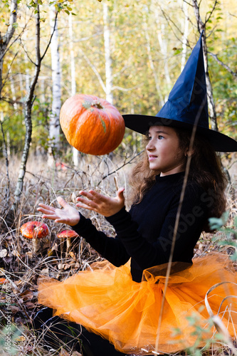 Little girl witch with magical pumpkin seating in a forest. Halloween concept.