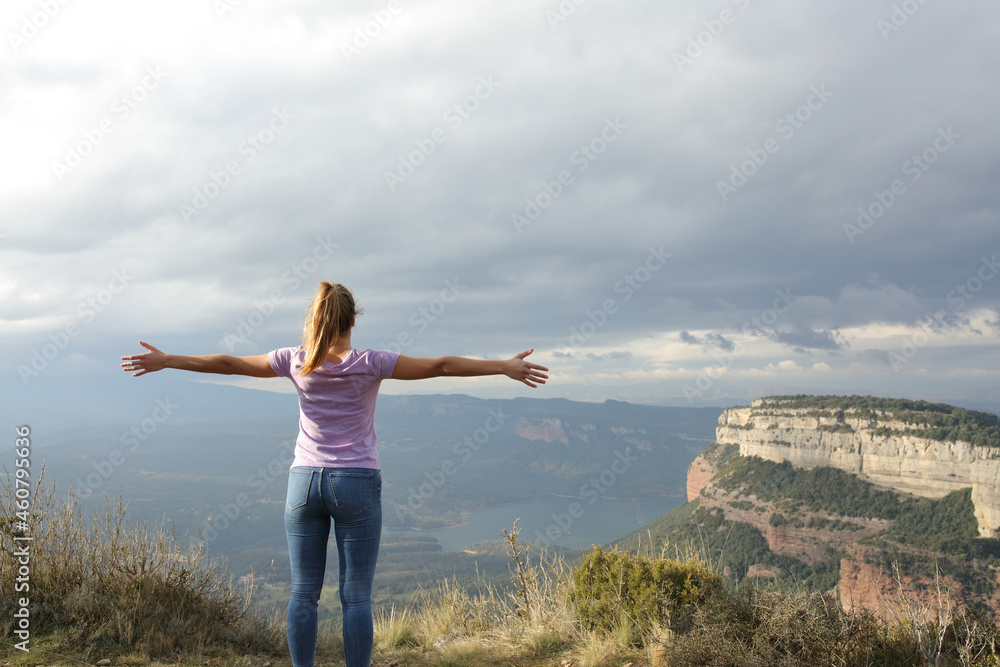 Back view of a woman outstretching arms in a cliff Back view of a woman outstretching arms in a cliff