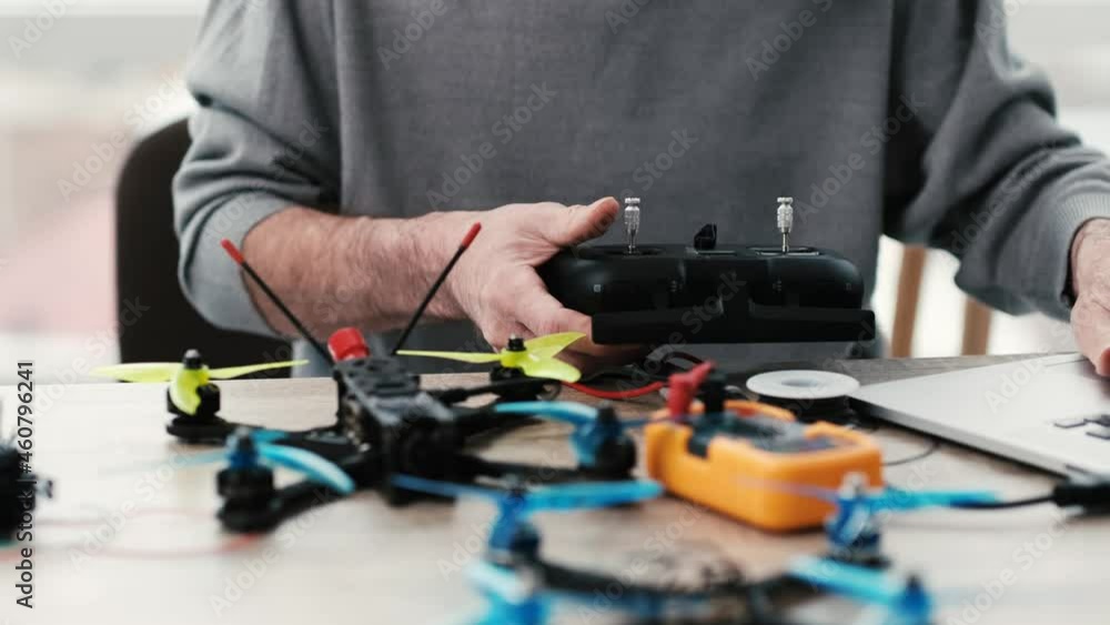 Man sitting by the table and programming quadcopter panel using laptop Man sitting by the table and programming quadcopter panel using laptop