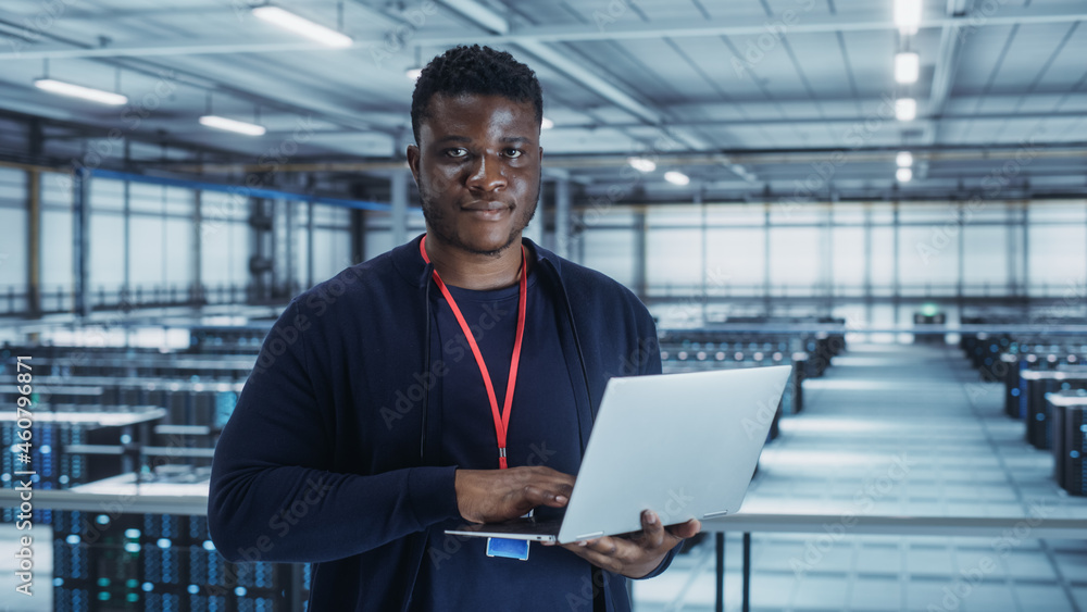 Portrait of a Data Center Engineer Using Laptop Computer. Server Room Specialist Facility with African American Male System Administrator Working with Data Protection Network for Cyber Security. Portrait of a Data Center Engineer Using Laptop Computer. Server Room Specialist Facility with African American Male System Administrator Working with Data Protection Network for Cyber Security.
